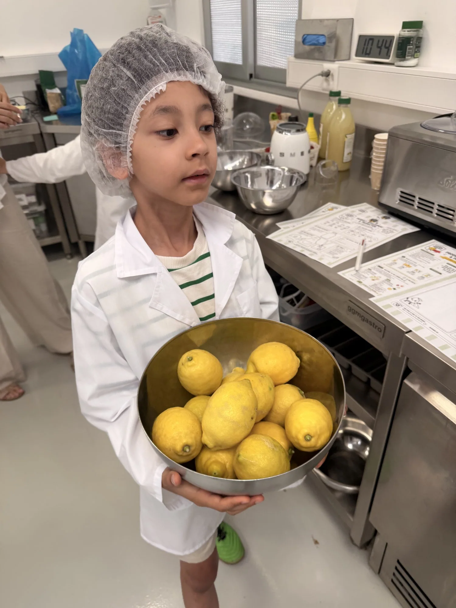A young chef in a hairnet holding a big bowl of fresh lemons